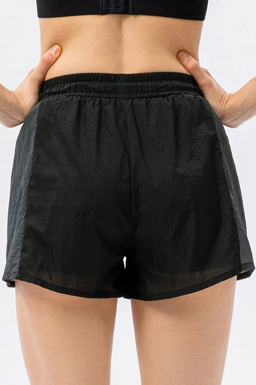 A model wears black color block active shorts with gray side panels, a gathered elastic waistband, and a relaxed, loose silhouette while posing with hands on hips.