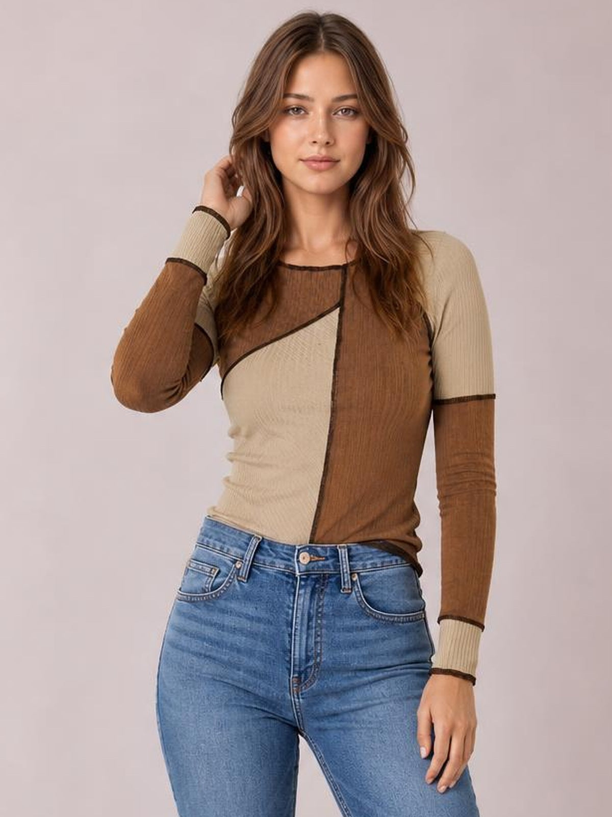Model poses in a fitted color block knit top with beige and brown ribbed panels, exposed seams, a round neck, and long raglan sleeves.