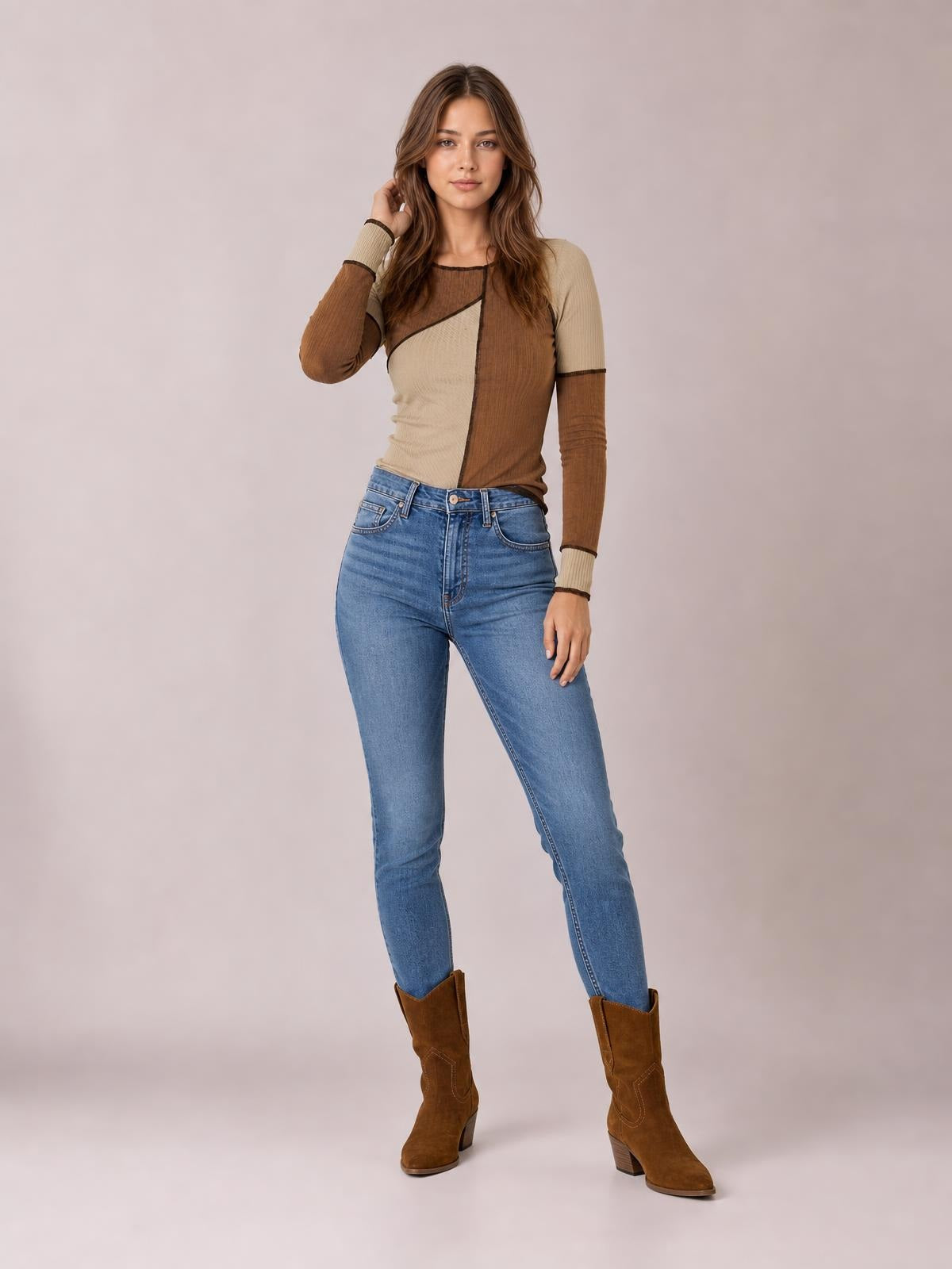 Model poses standing with one hand in her hair, wearing a fitted brown and beige color block knit top with ribbed texture, exposed seams, and long sleeves.