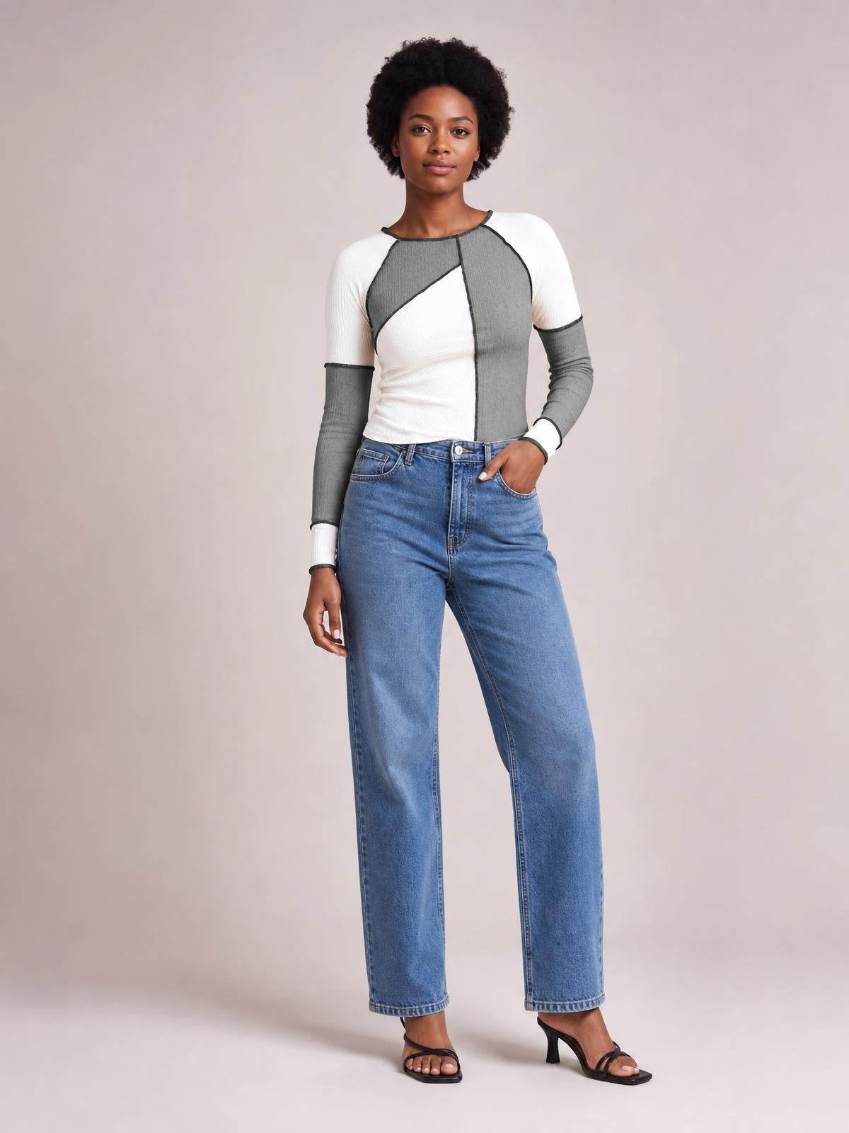 Model poses with one hand in her pocket wearing a fitted color block knit top with a round neck, ribbed texture, long raglan sleeves, and exposed seams.
