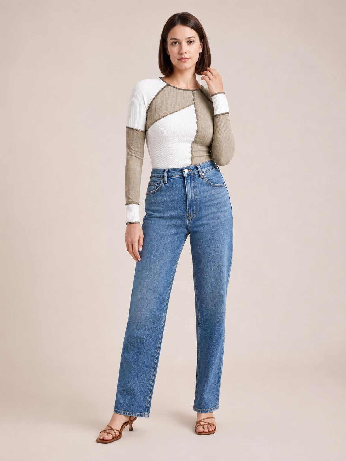 A model poses with one hand near her hair in a taupe-and-white color block knit top with a round neck, ribbed texture, exposed seams, and long raglan sleeves.