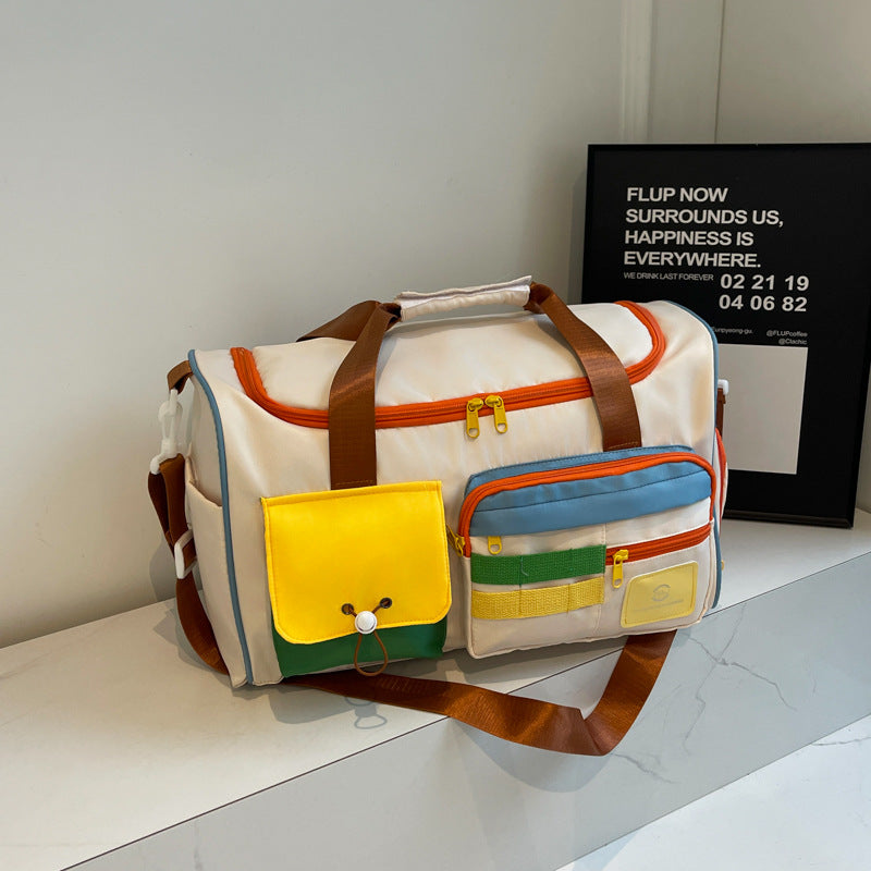 Large beige color-block travel bag with brown top handles, orange zippers, bright yellow, blue and green accents, multiple exterior pockets, and a shoulder strap.