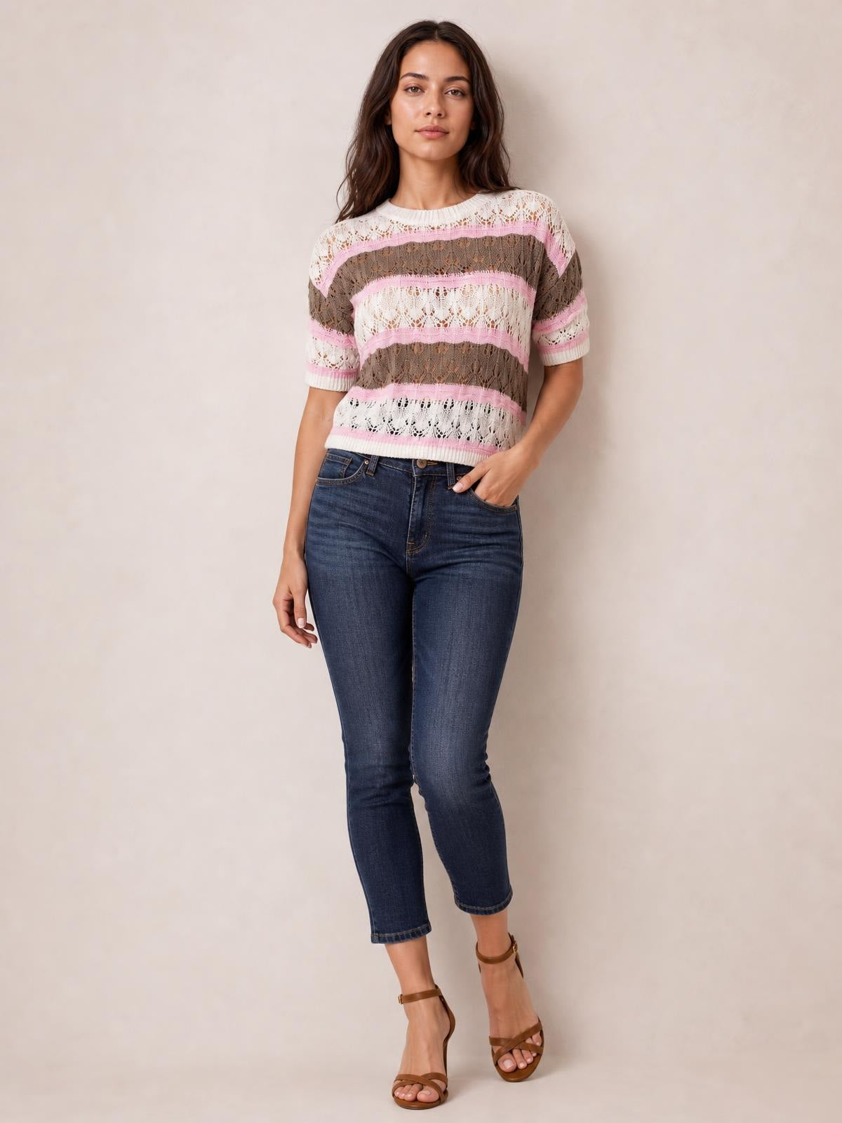 Model wearing a pink, brown, and white color block openwork sweater with half sleeves, crew neckline, ribbed trim, and a relaxed silhouette, posing with one hand in her pocket.