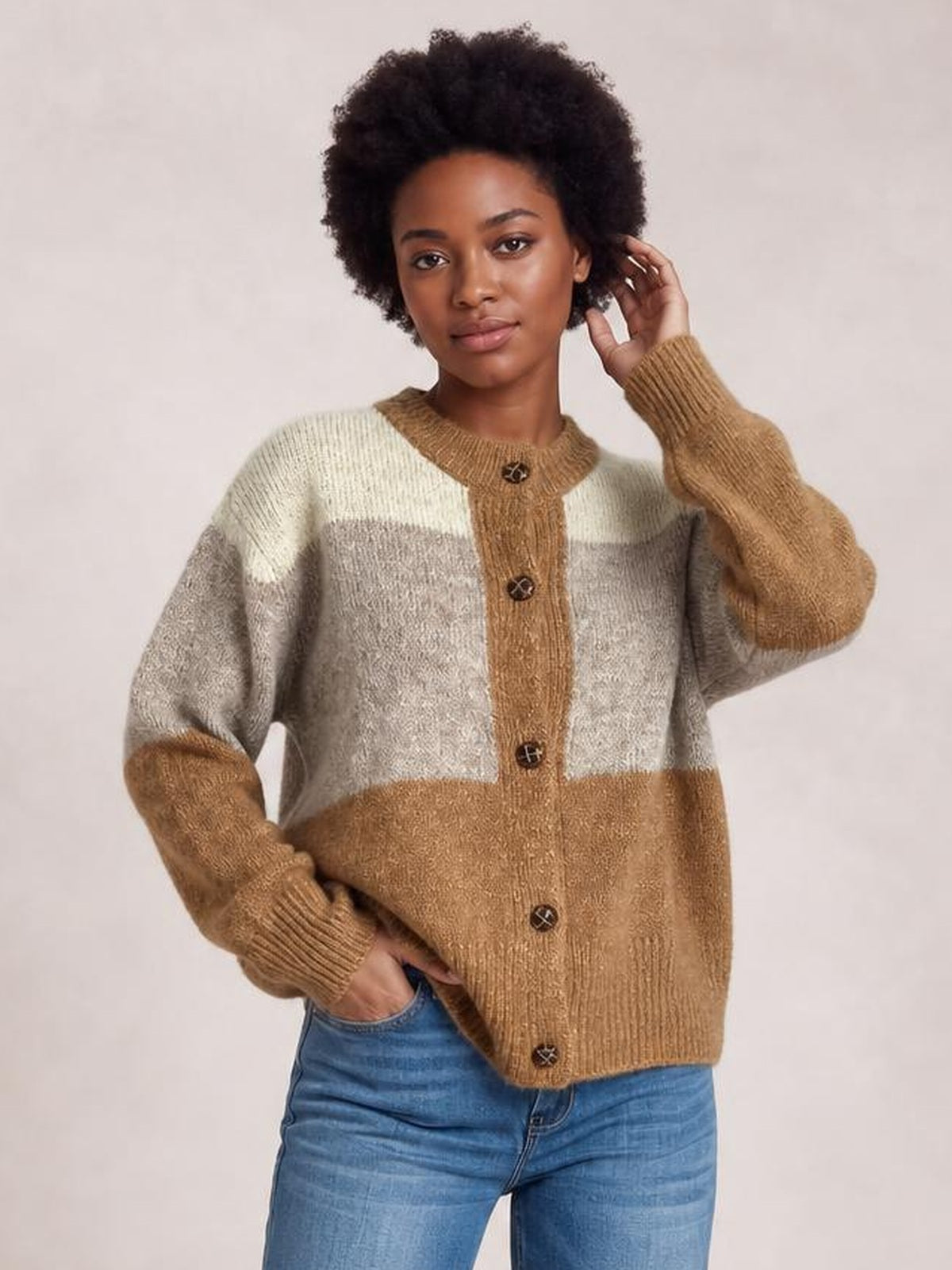 Model poses in a relaxed color block cardigan with a round neck, button-up front, camel, beige, and gray panels, long sleeves, and ribbed trims.