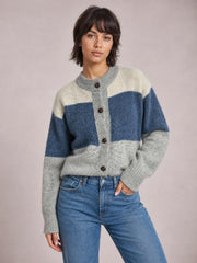 Model poses with one hand in her jeans pocket, wearing a relaxed color block cardigan with a round neck, button front, long sleeves, and blue, gray, and cream sections.