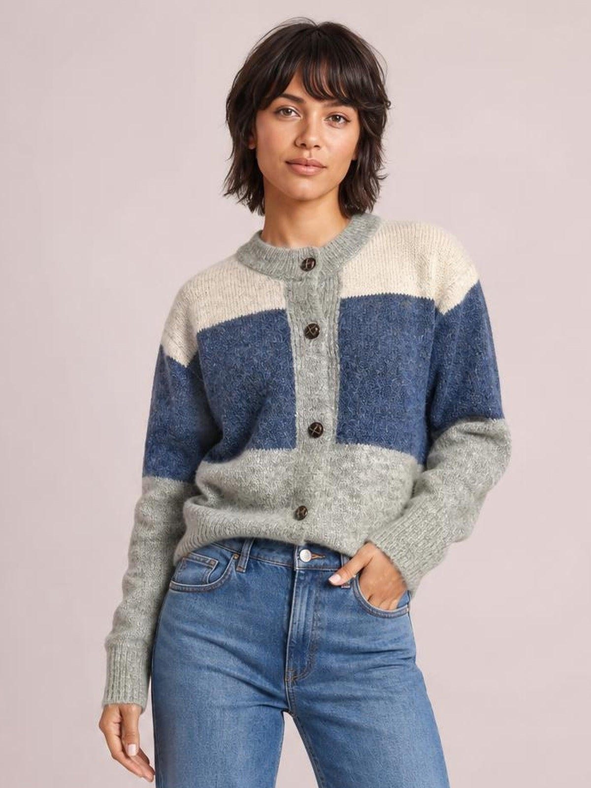 Model poses in a blue, cream, and gray color block round neck button-up cardigan with ribbed trim, long sleeves, and a relaxed silhouette.