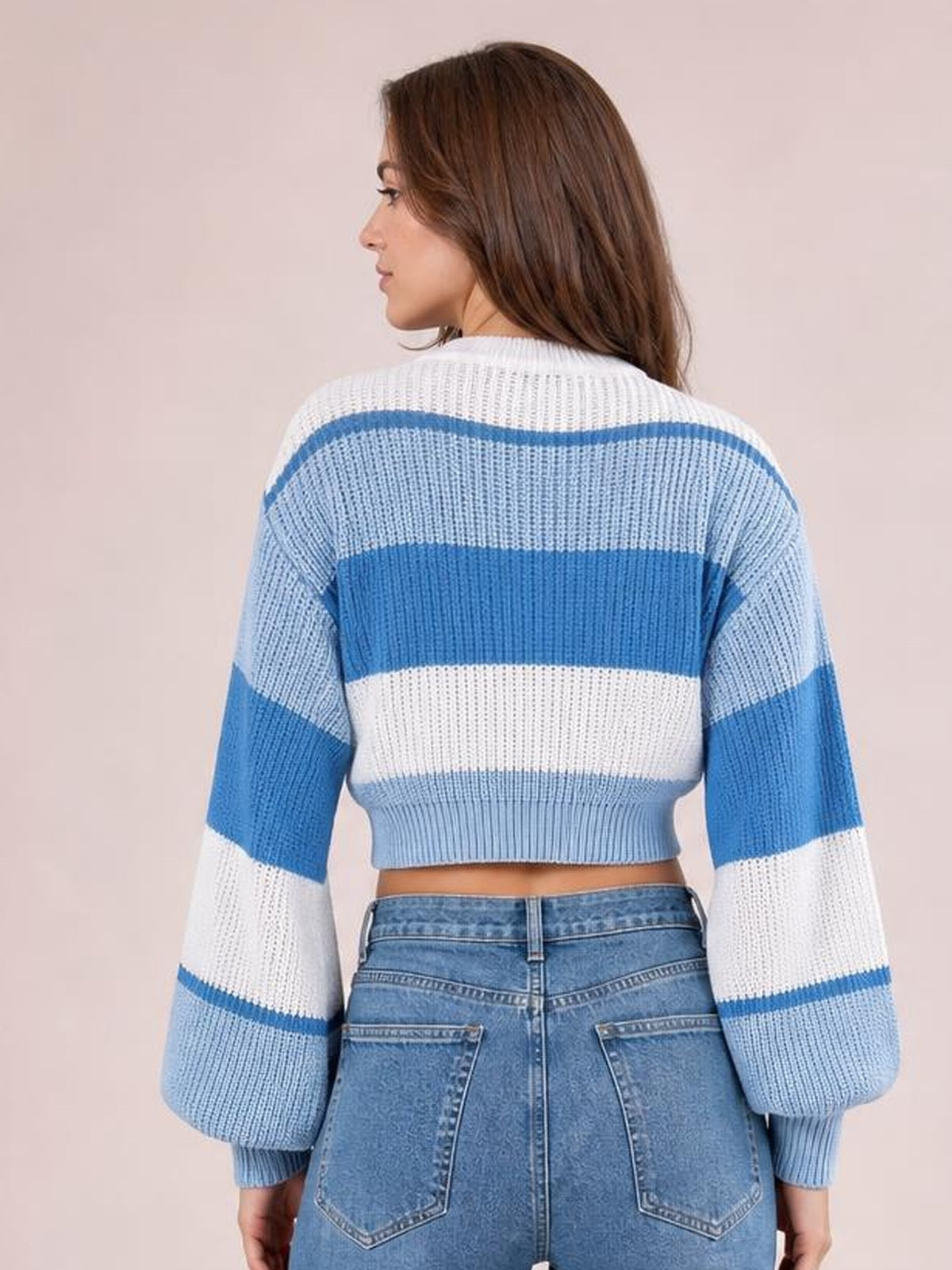 A model faces away wearing a blue and white color-block cropped sweater with a round neck, long sleeves, ribbed cuffs, and a fitted hem.