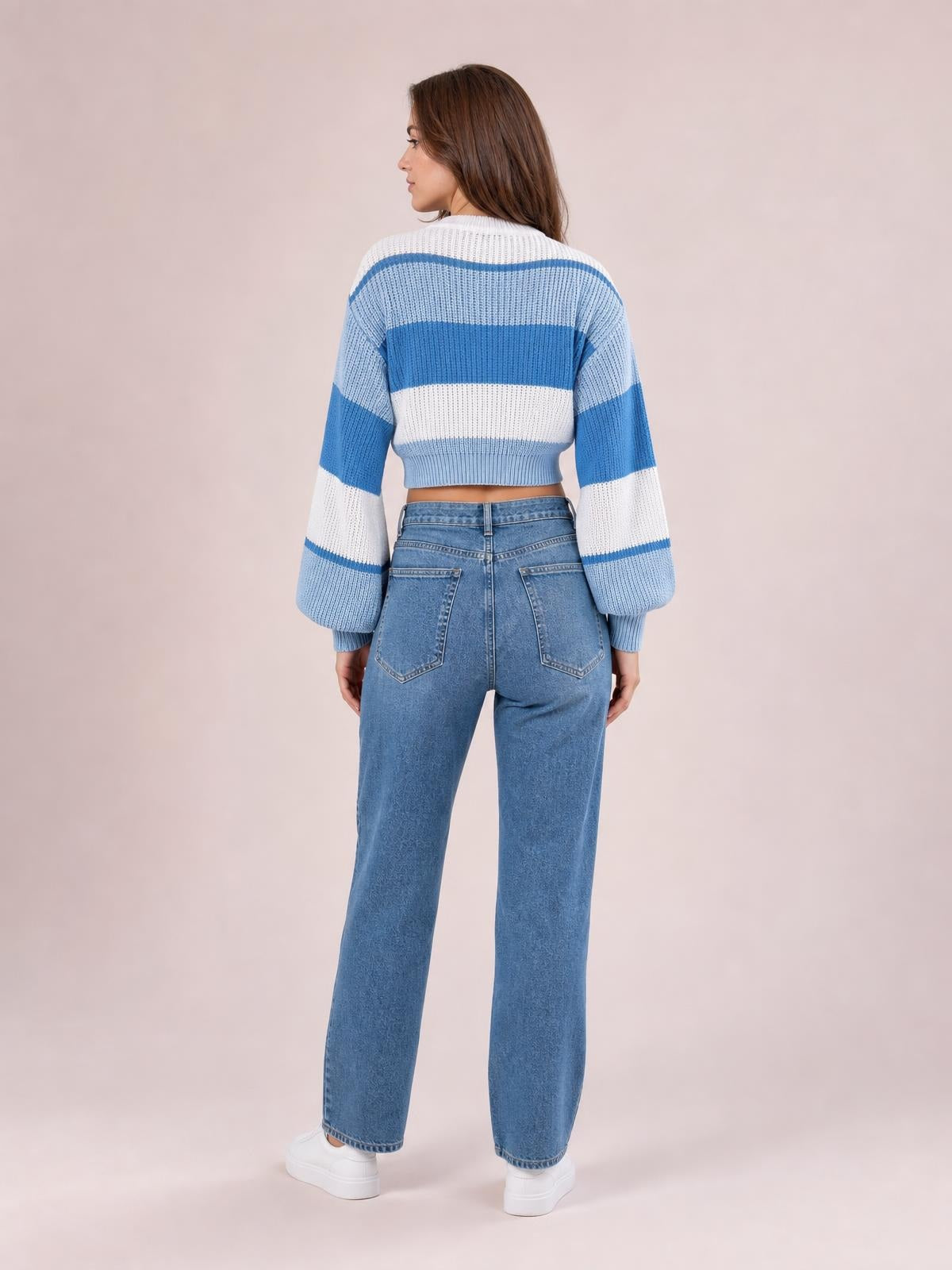 A model stands facing away in a blue and white color block round neck cropped sweater with rib-knit construction and long sleeves.