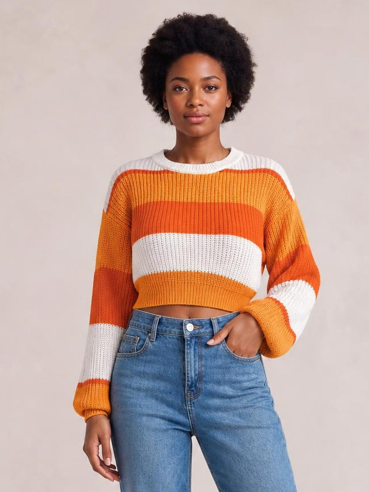 Model wearing a color-block cropped sweater with a round neck, orange and white horizontal stripes, ribbed knit construction, and long sleeves.