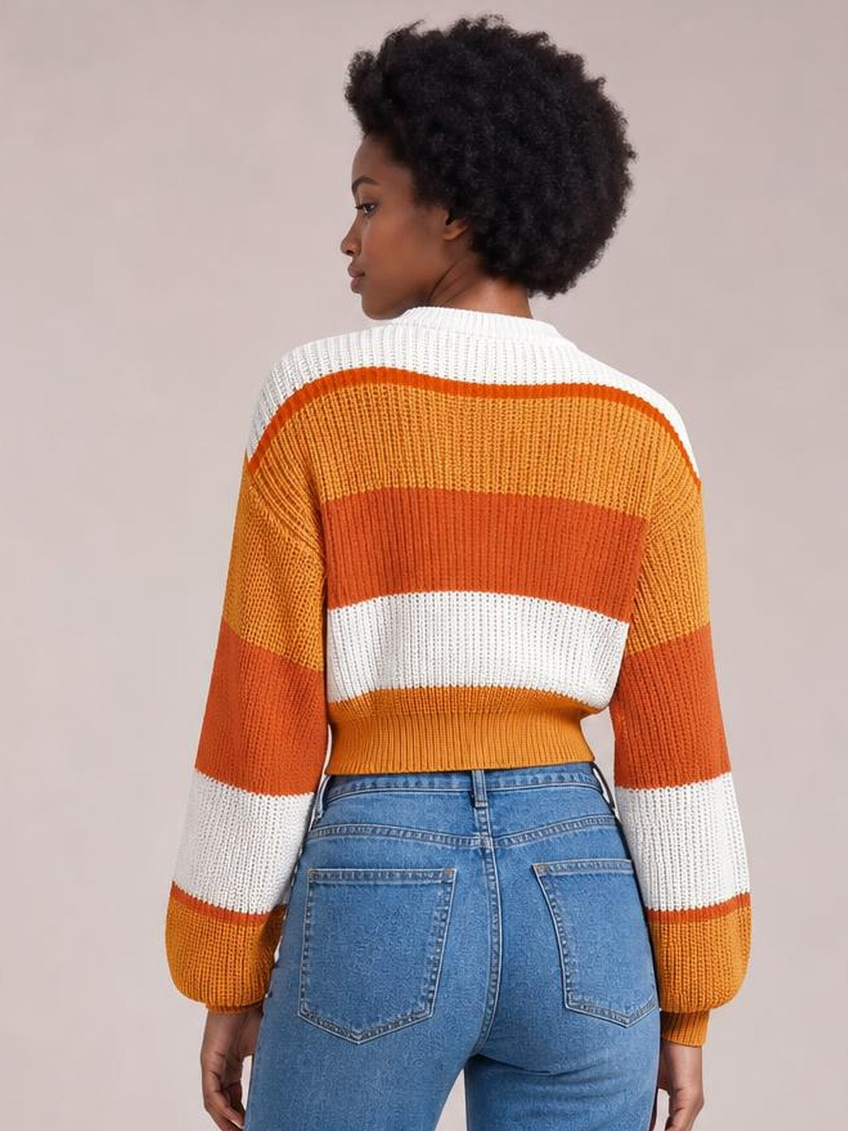 Model shown from the back wearing a cropped color block sweater with a round neck, orange and white rib-knit panels, and long sleeves.