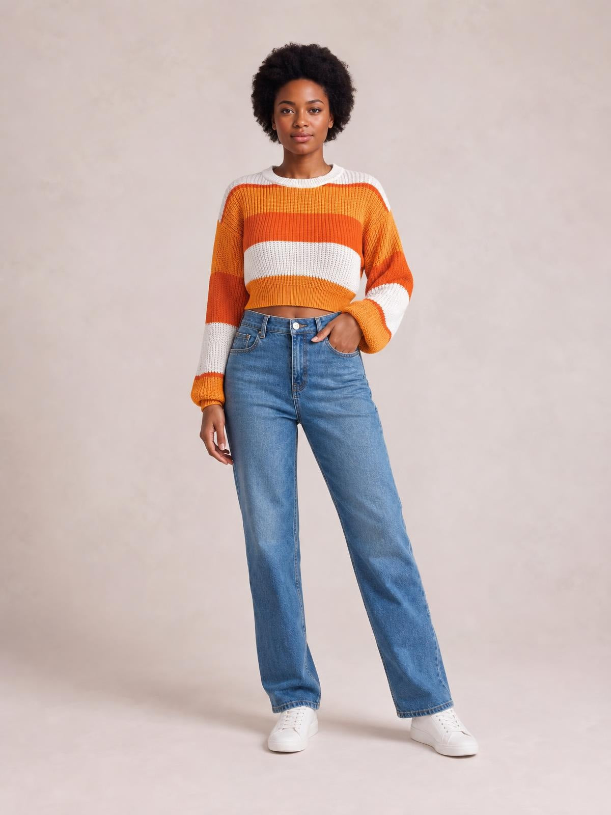 Model poses in a color-block cropped sweater with a round neck, orange and white stripes, ribbed trim, and long sleeves.