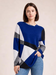 A model stands in a relaxed pose wearing a blue, white, gray, and black color block round neck T-shirt with long sleeves and a loose silhouette.