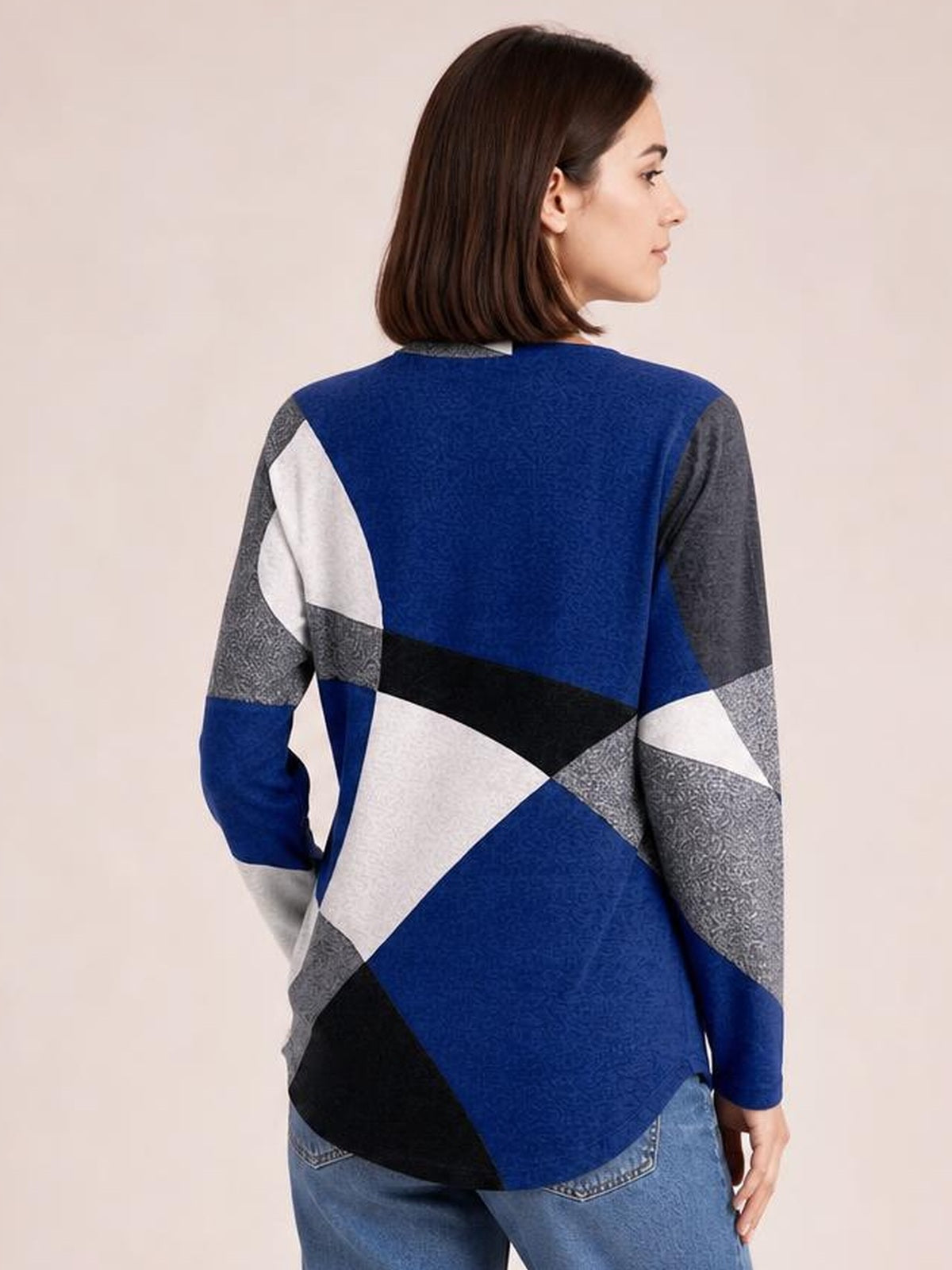 A model poses in a relaxed color block round neck T-shirt with long sleeves and geometric blue, gray, white, and black panels, shown from the back.
