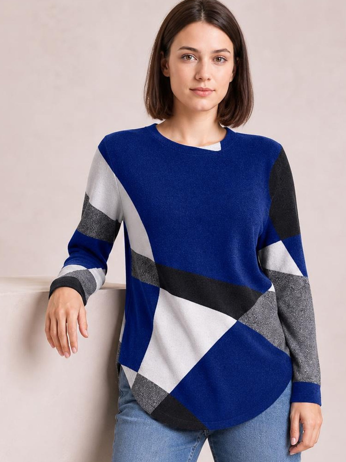 A woman poses in a blue Color Block Round Neck T-Shirt with long sleeves, geometric white, gray, and black panels, and a relaxed curved-hem silhouette.