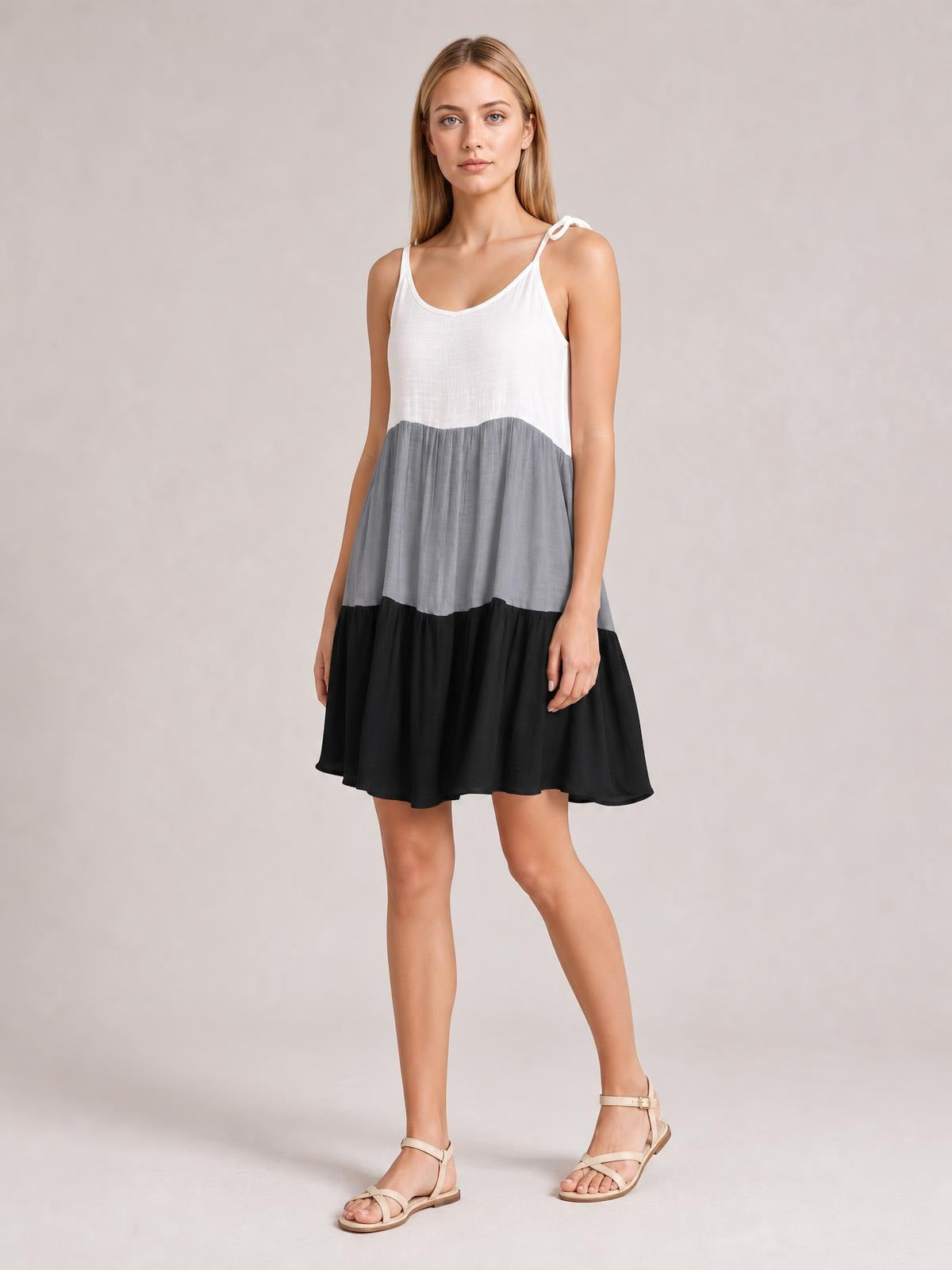 A model poses in a semi-sheer color block cover-up dress with white spaghetti straps, gray and black tiers, a relaxed A-line silhouette, and a gently gathered skirt.