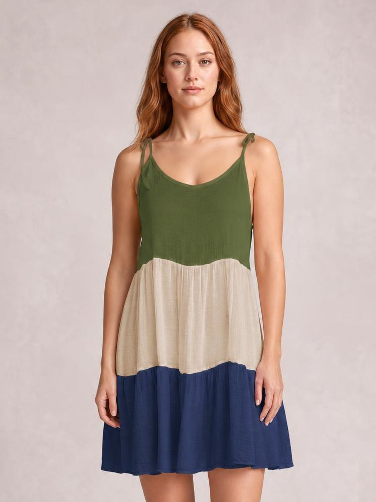 A model stands in a semi-sheer color block cover-up dress with green spaghetti straps, a cream middle panel, navy tiered skirt, and relaxed silhouette.