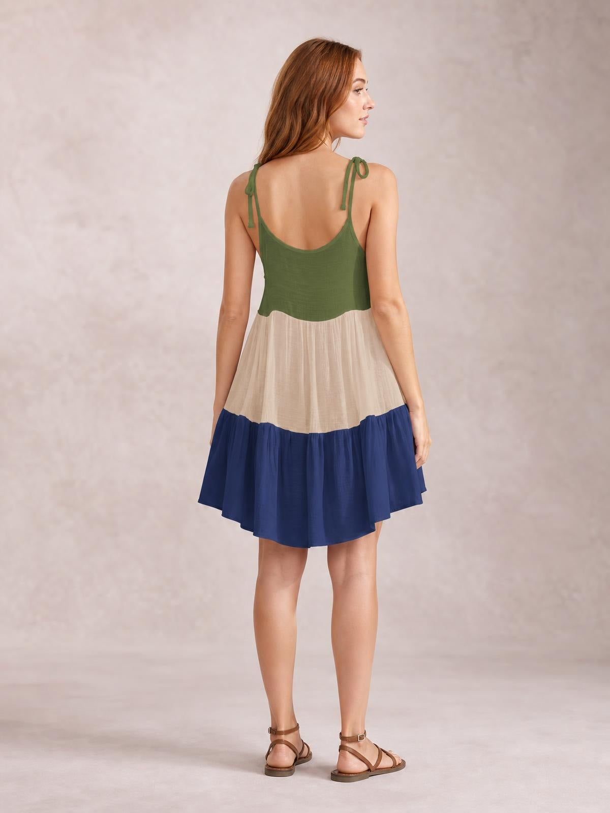 A model stands facing away in a semi-sheer color block cover-up dress with green spaghetti tie straps, a cream panel, and a flowing navy skirt.