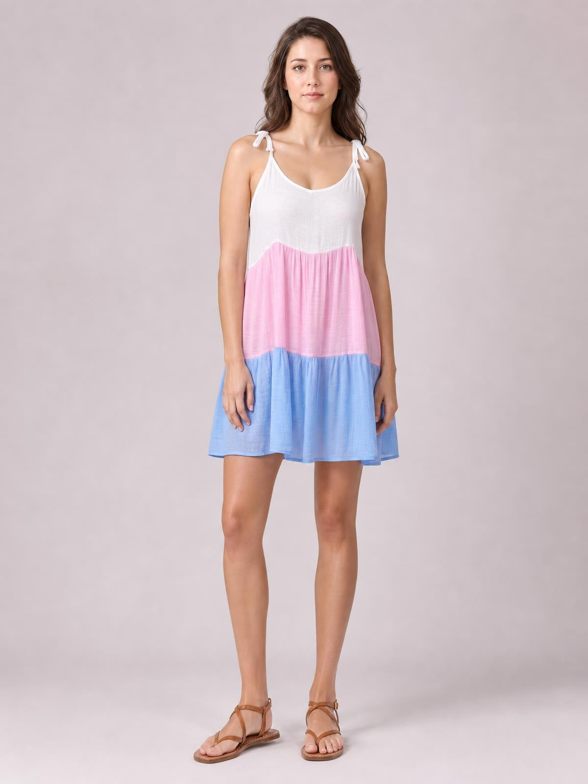A model stands in a semi-sheer color block spaghetti strap cover-up dress with white, pink, and blue gathered tiers and a relaxed above-knee silhouette.