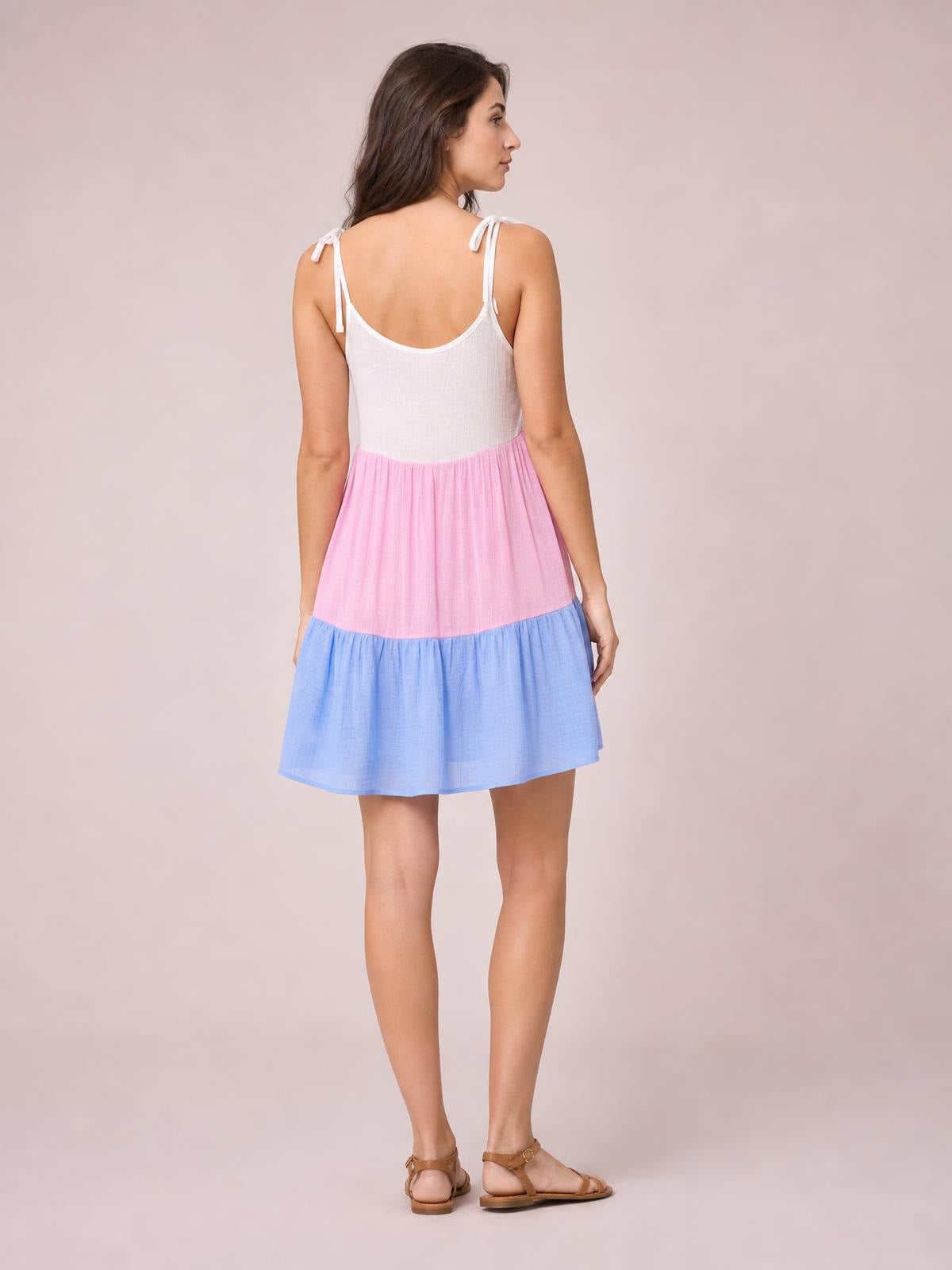 Model shown from the back in a semi-sheer color block cover-up dress with white spaghetti straps, a pink tier, and a blue flared skirt.