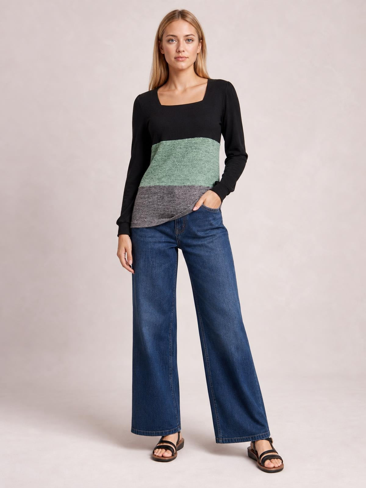 Model stands with one hand in her jeans pocket wearing a black, sage green, and gray color-block T-shirt with a square neck, long sleeves, and curved hem.