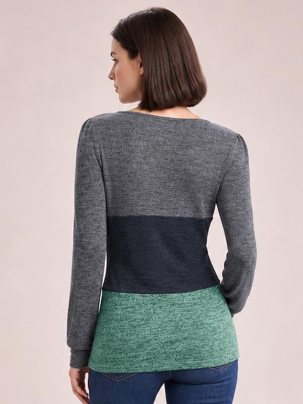 A model turns slightly to show the back of a color block long sleeve T-shirt with gray, navy, and green panels in a fitted silhouette.