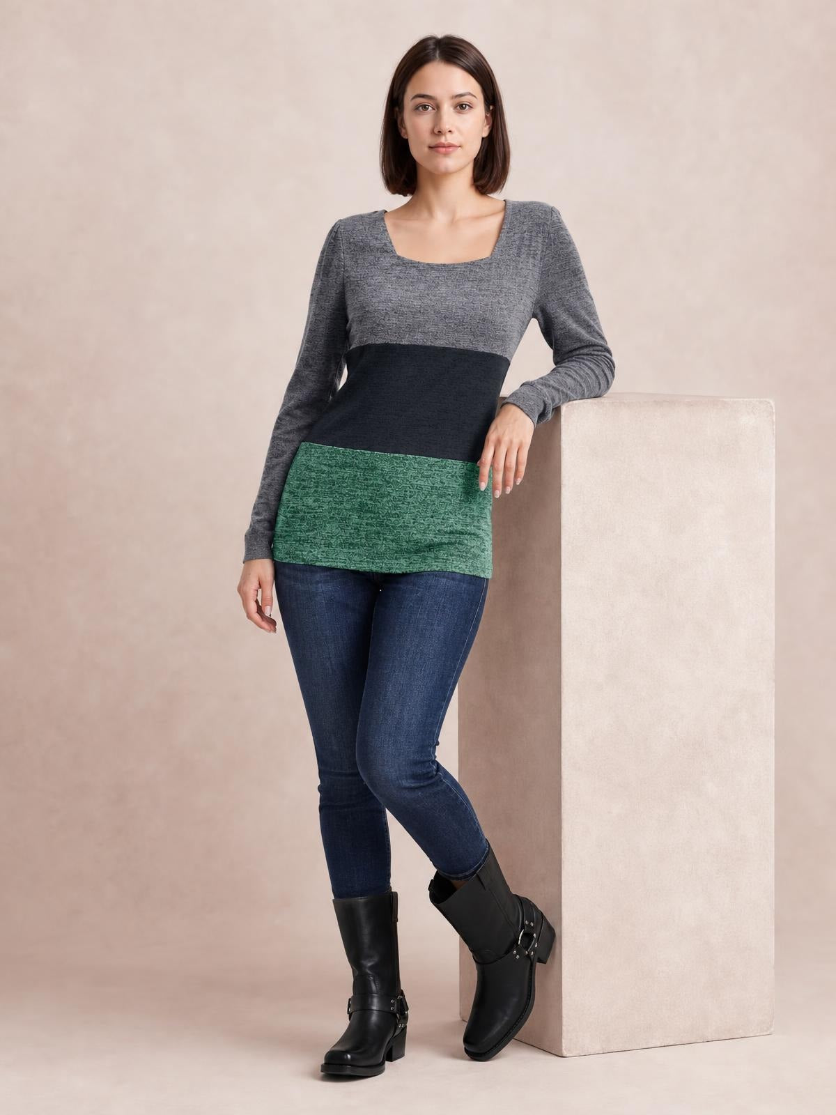 Model wears a color block square neck long sleeve T-shirt with gray, black, and green panels in a fitted silhouette, leaning with one hand and crossed legs.