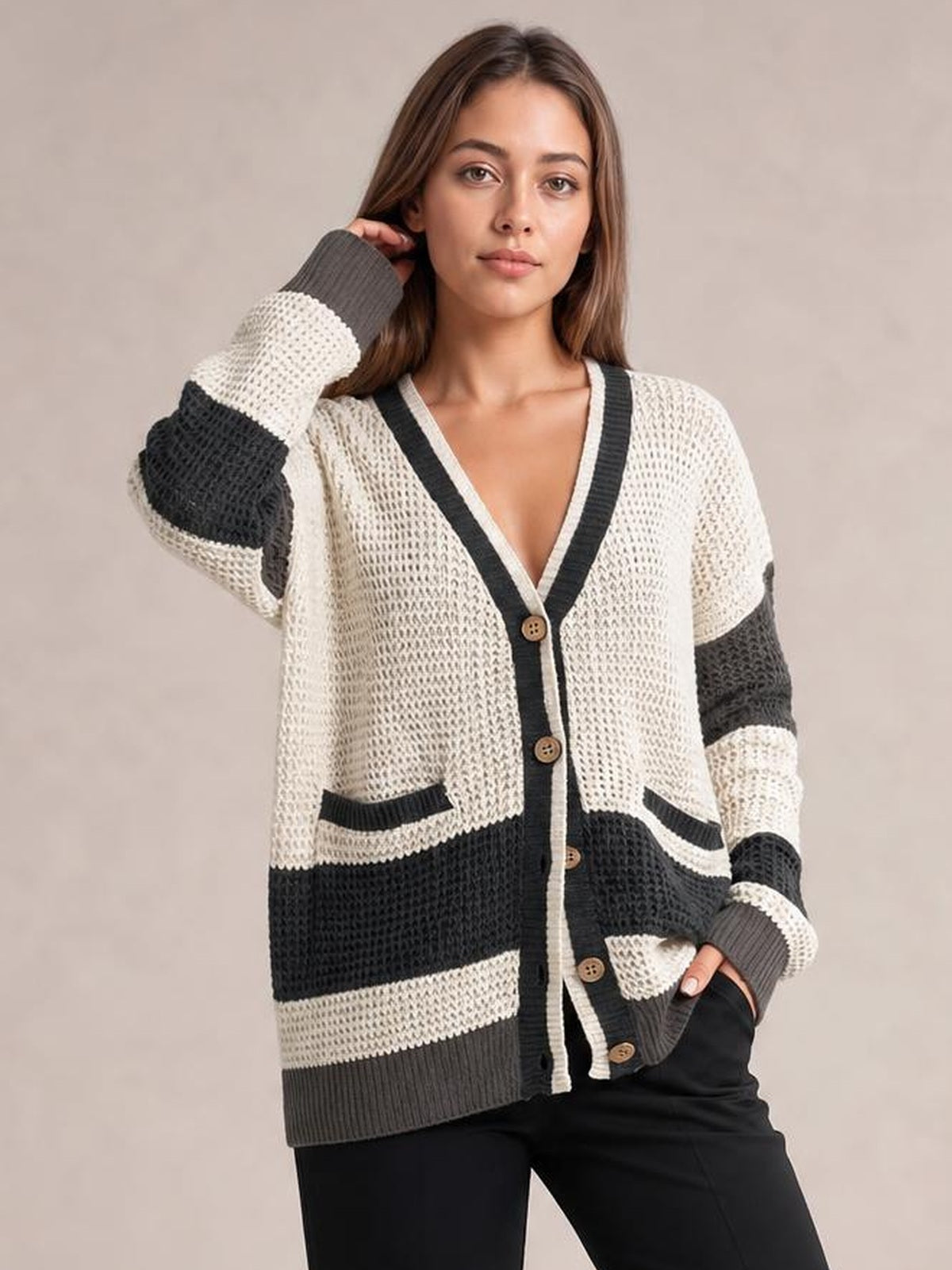 Model poses in a relaxed color block V-neck cardigan with waffle-knit texture, cream and charcoal panels, button front, contrasting trim, and two pockets.