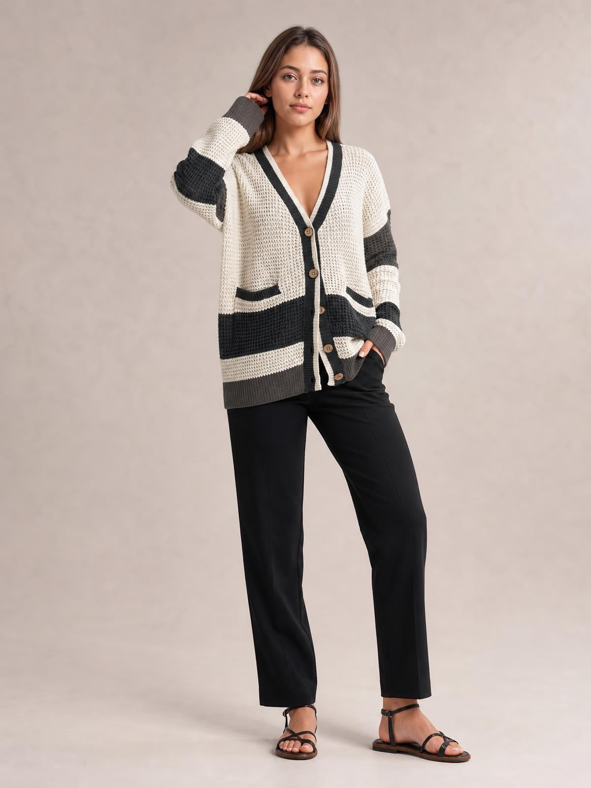 A model poses in a relaxed stance wearing a cream and black color block V-neck cardigan with waffle-knit texture, buttons, pockets, and ribbed trim.