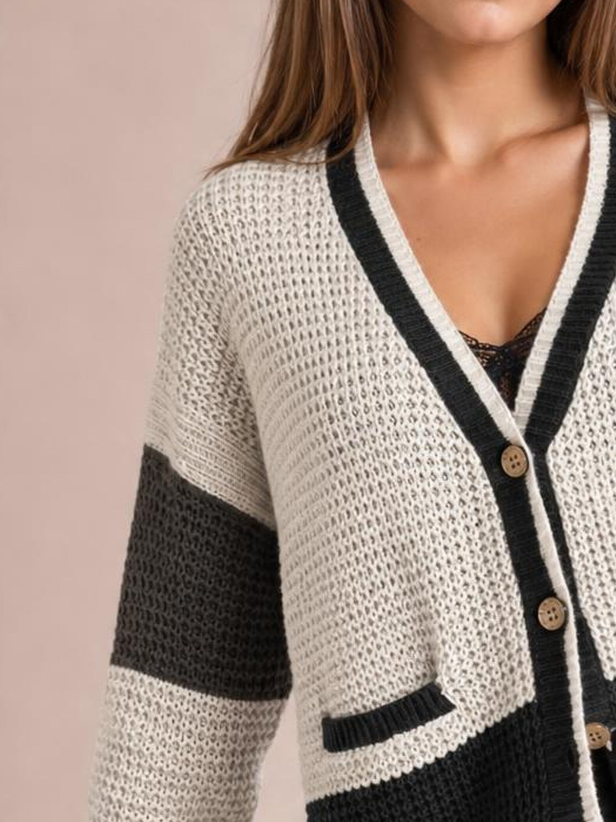 A model wears a cream and black color block V-neck cardigan with waffle knit texture, button front, contrasting sleeve panels, and a rib-trimmed pocket.
