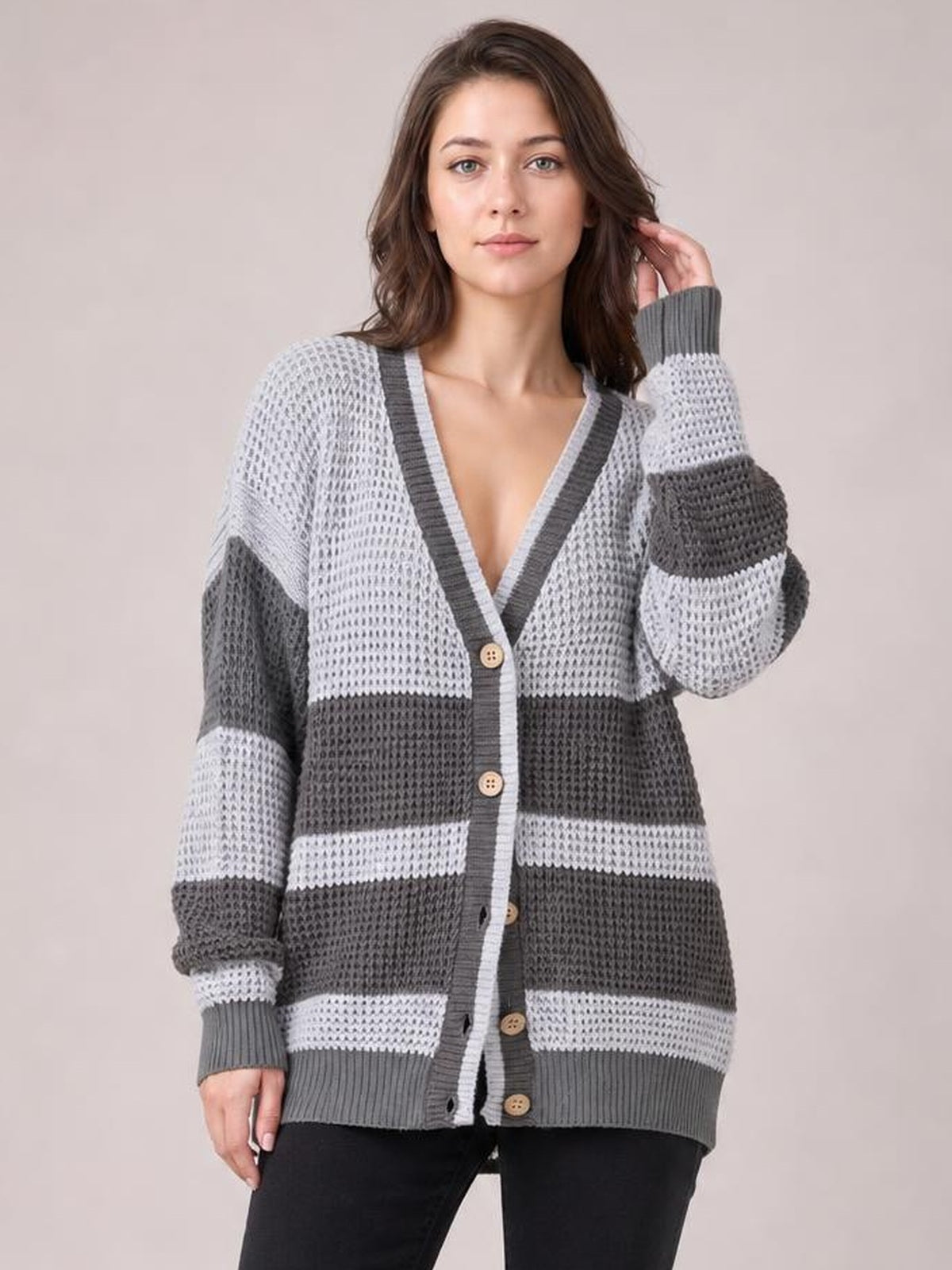 Model poses in a gray and white color block V-neck cardigan with waffle-knit texture, button front, striped sleeves, ribbed trim, and a relaxed silhouette.