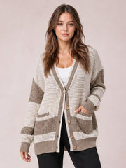 Model poses in a relaxed color block V-neck cardigan with a waffle-knit texture, button front, contrasting trim, striped sleeves, ribbed cuffs, hem, and front pockets.