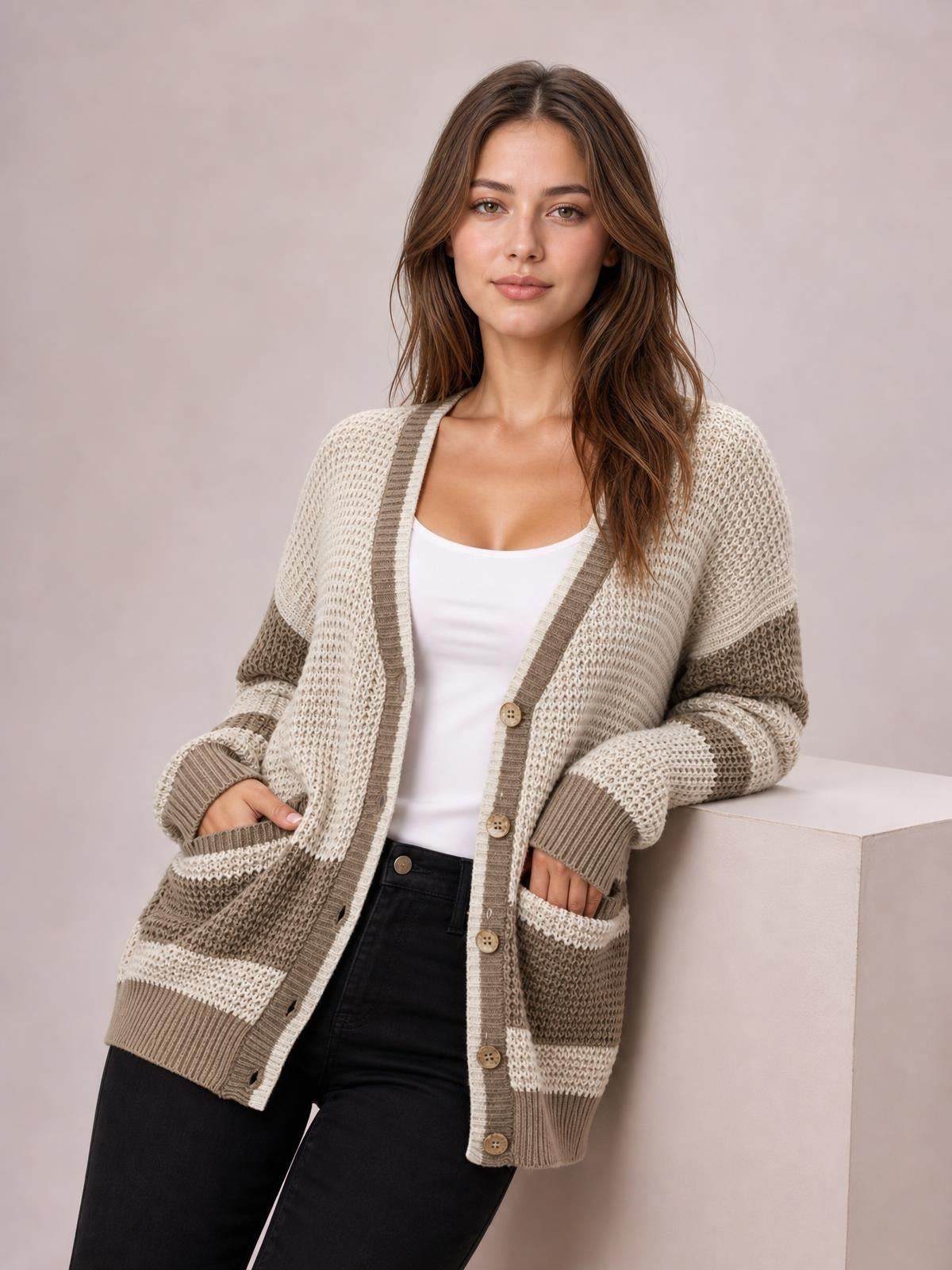 Model wears a relaxed color block V-neck cardigan in cream and taupe, with waffle-knit texture, button front, striped sleeves, ribbed cuffs, and patch pockets.
