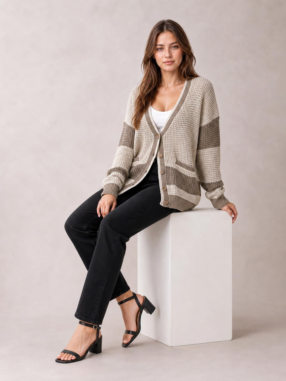 Model seated in a color block V-neck cardigan with waffle-knit texture, button front, patch pockets, striped sleeves, and a relaxed silhouette.