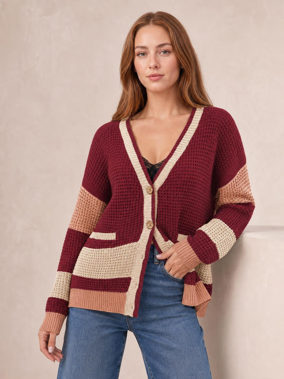 Model wears a burgundy, cream, and pink color-block waffle-knit cardigan with a V-neck, button front, pockets, striped sleeves, and relaxed silhouette.