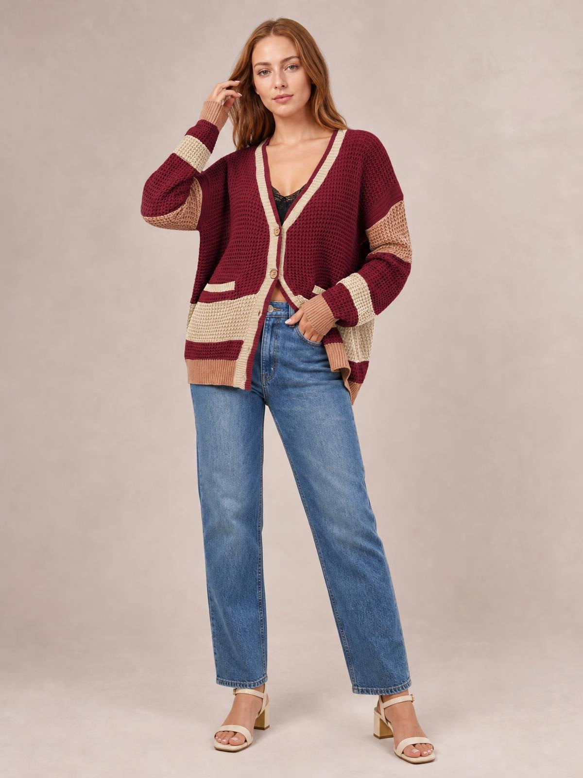Model wearing a burgundy and cream color-block V-neck cardigan with waffle-knit texture, button front, contrast seams, pockets, and a relaxed silhouette.
