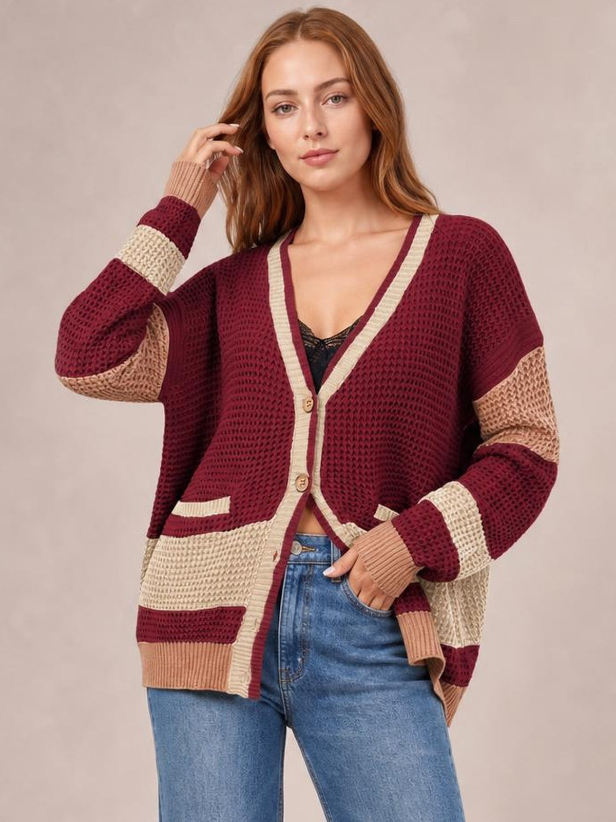Model poses in a burgundy, cream, and tan color block V-neck cardigan with waffle-knit texture, button front, long sleeves, ribbed cuffs, and pockets.