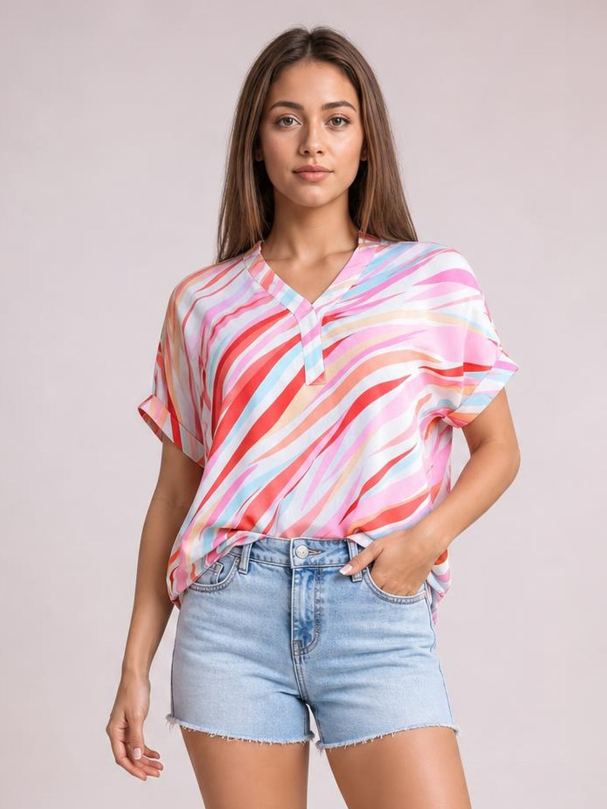 Model wearing a loose color block blouse with a V-neck, short half sleeves, and flowing pink, red, blue, and white abstract stripes.