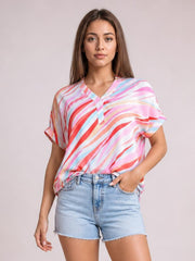 Model wearing a loose color block blouse with a V-neck, short half sleeves, and flowing pink, red, blue, and white abstract stripes.