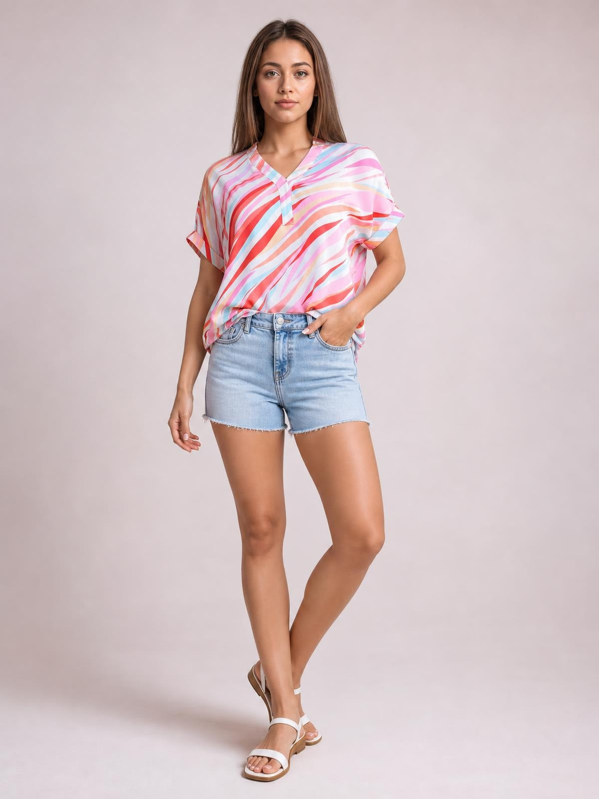 Model poses in a colorful striped V-neck blouse with short sleeves, a relaxed silhouette, and contrasting trim at the neckline and sleeve cuffs.