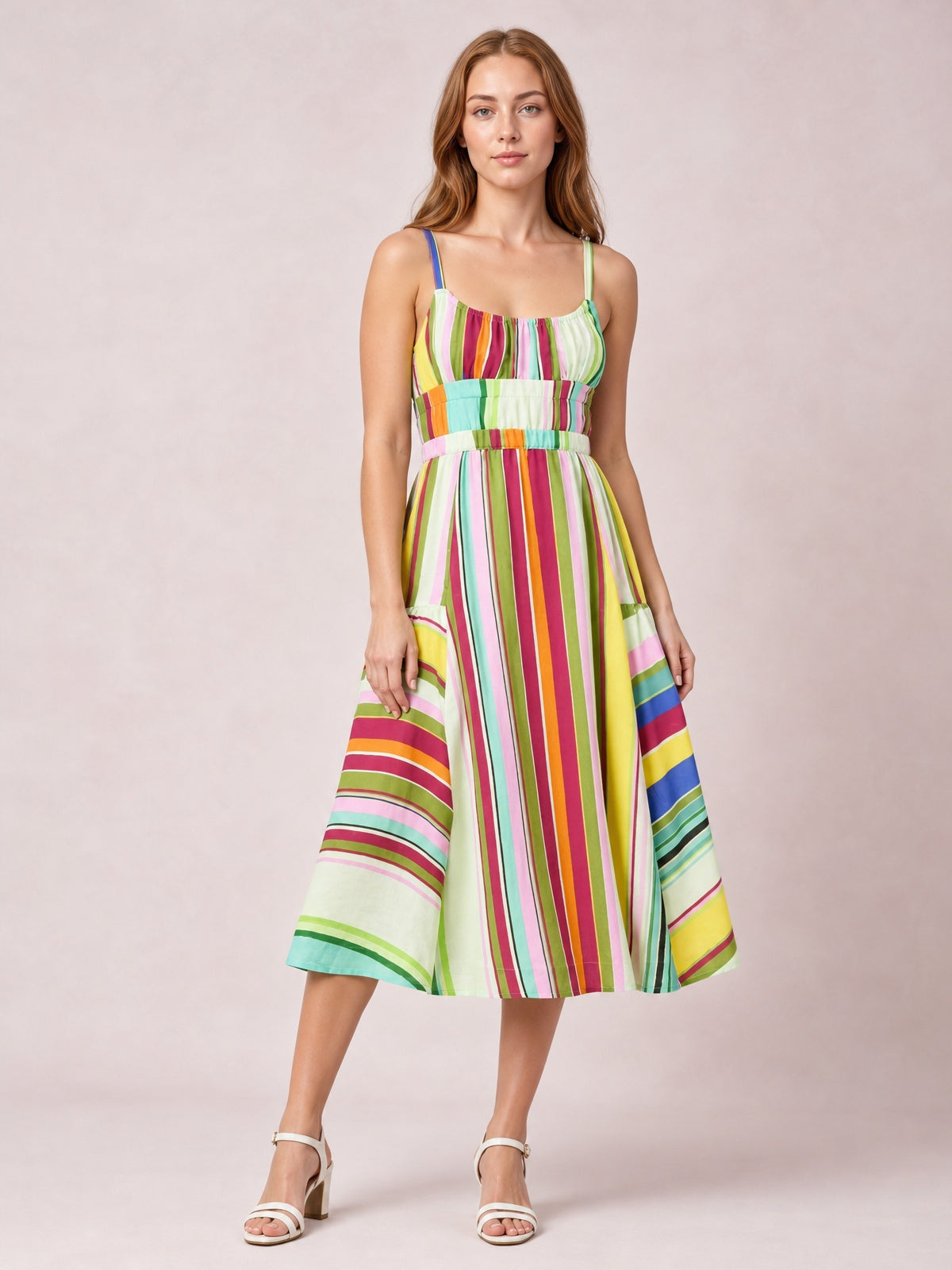 Model wears a colorful striped spaghetti strap midi dress with a gathered neckline, defined waistband, mixed vertical and horizontal stripes, and a gently flared skirt.
