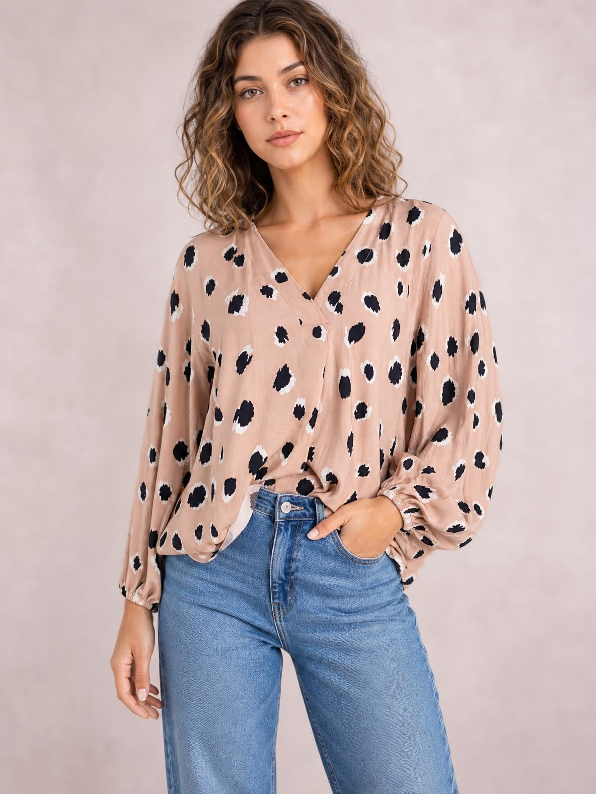 Model wearing a blush pink contrast animal print V-neck long sleeve blouse with a relaxed silhouette and gathered cuffs, posing with one hand in her jeans pocket.