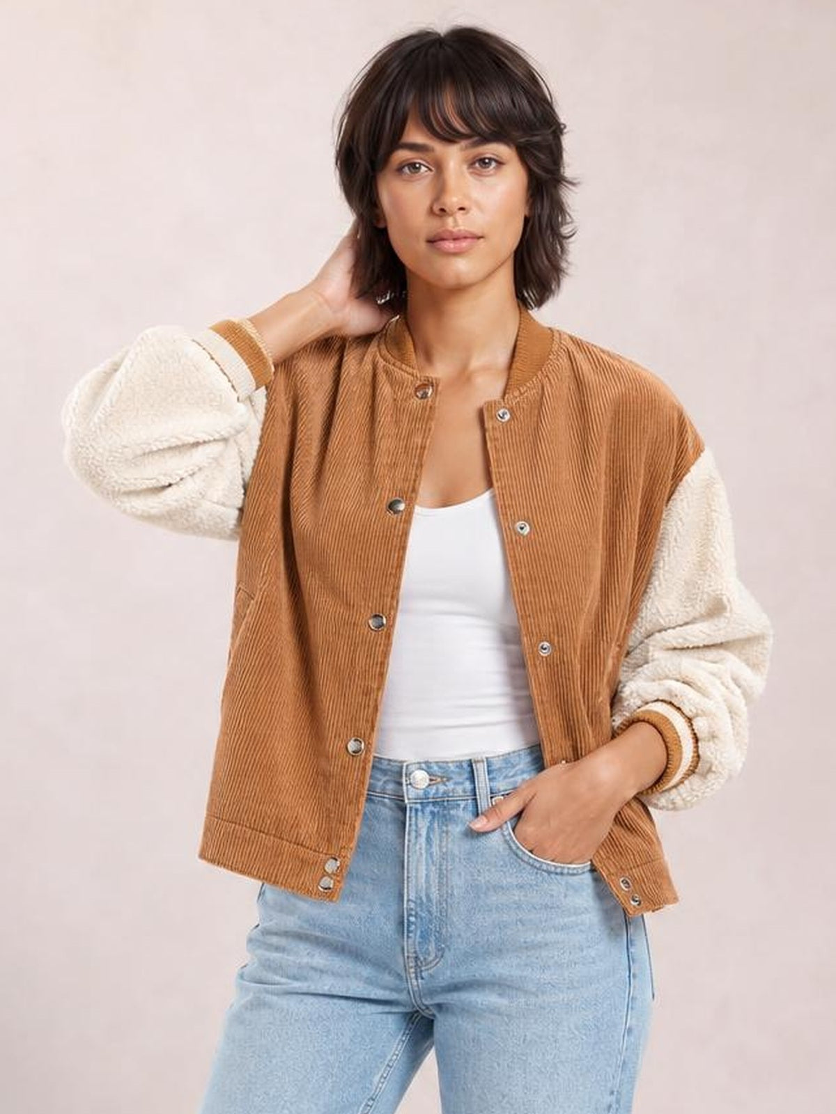 Model poses in a brown corduroy baseball collar snap-down jacket with contrasting cream sherpa long sleeves, ribbed cuffs, and a relaxed silhouette.
