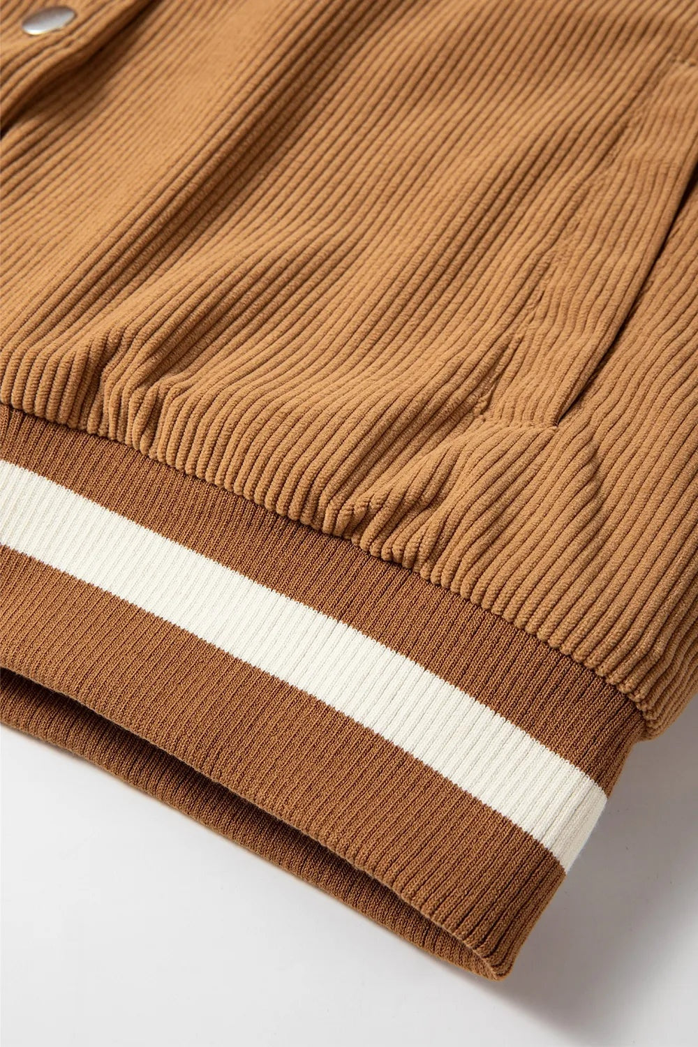 Close-up of a tan corduroy jacket showing textured fabric, a ribbed brown hem, and a contrasting white horizontal stripe.