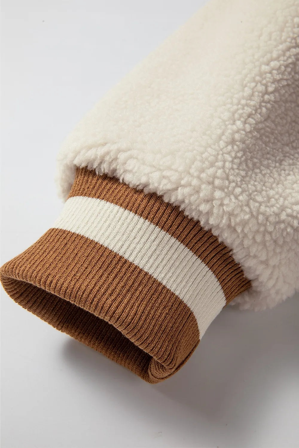 Close-up of a cream textured long sleeve jacket with a brown ribbed cuff featuring a contrasting white stripe and neatly finished construction.