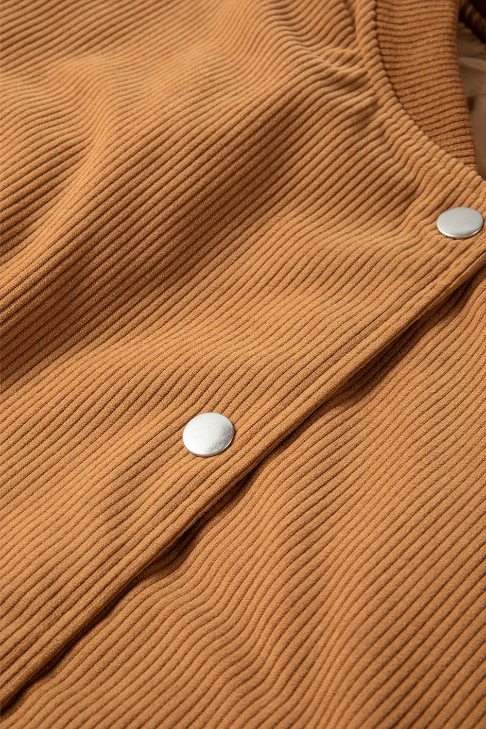 Close-up of a tan ribbed jacket front showing the snap-down closure, two silver metal snaps, and textured fabric construction.