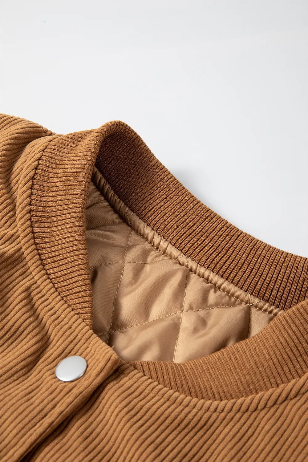 Close-up of a camel-brown jacket showing its ribbed baseball collar, silver snap closure, long sleeves, and quilted satin lining.
