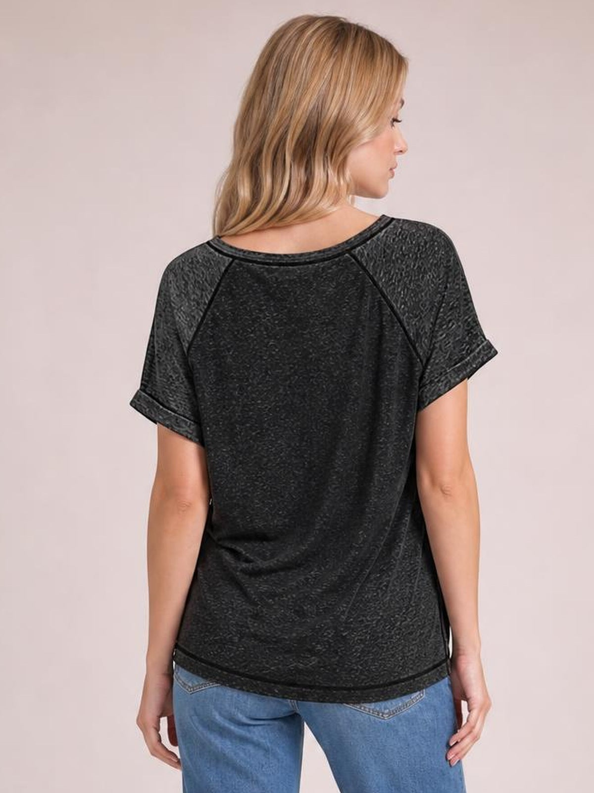 A model faces away in a black contrast short sleeve T-shirt with rolled cuffs, raglan-style seams, a relaxed silhouette, and a rounded back neckline.