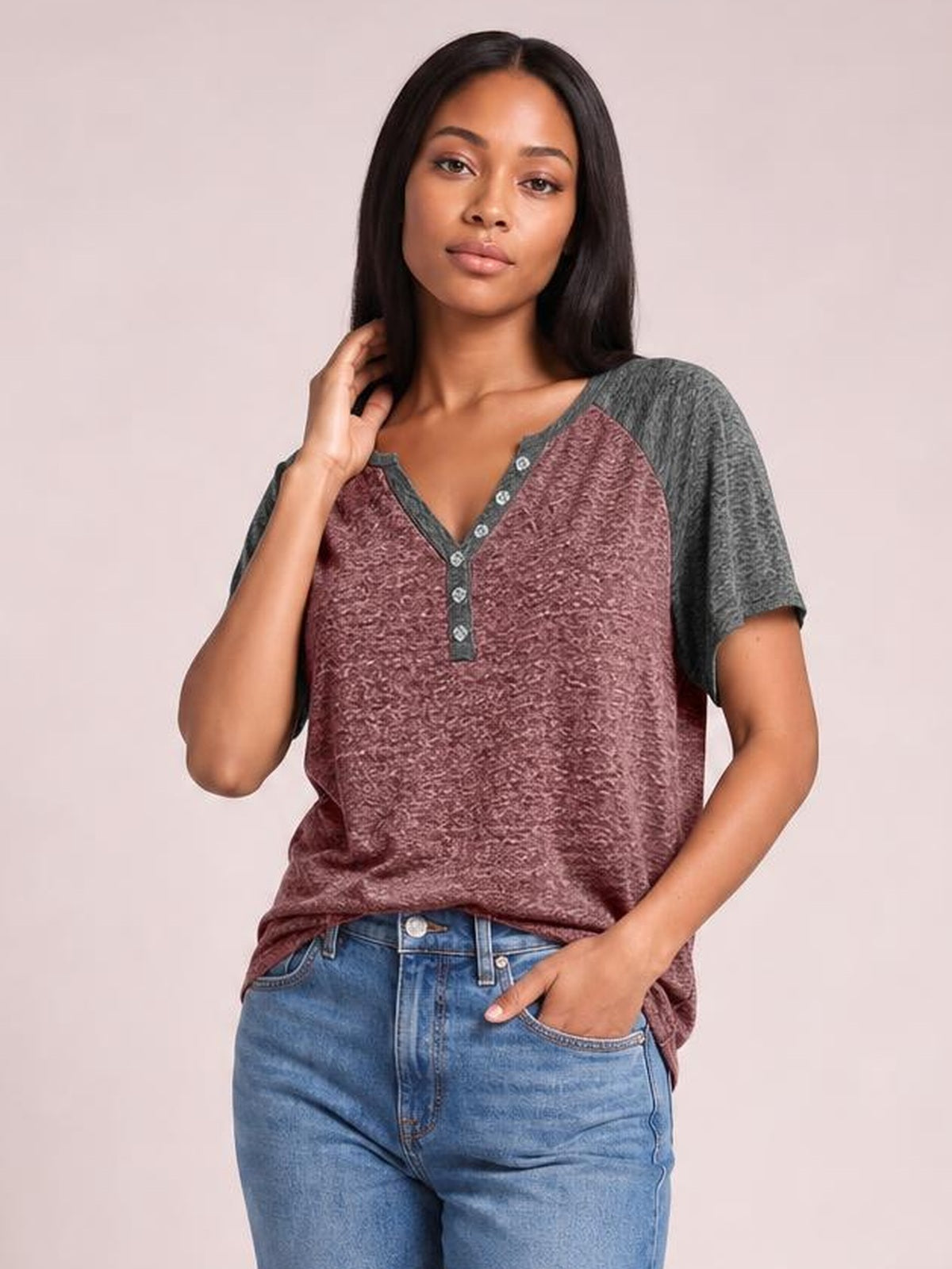Model poses in a burgundy contrast notched short sleeve T-shirt with gray sleeves, a V-neckline, decorative button placket, and relaxed silhouette.