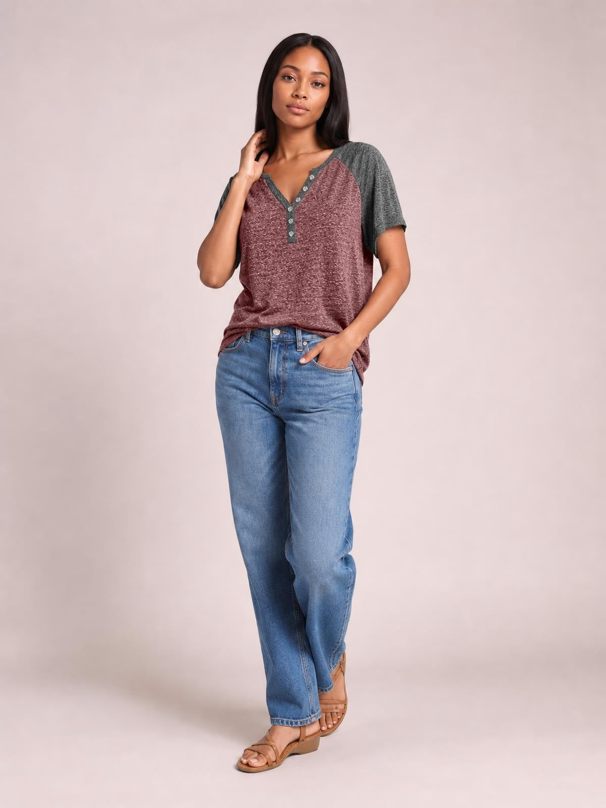 Model wears a burgundy and charcoal contrast notched short sleeve T-shirt with decorative buttons and a relaxed silhouette, posing with one hand in her jeans pocket.