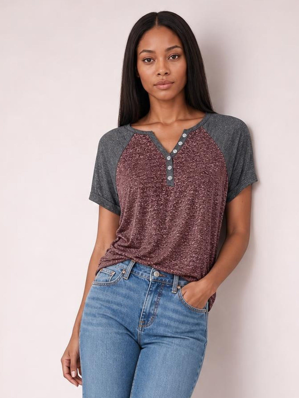 Model wearing a burgundy contrast notched short sleeve T-shirt with charcoal sleeves, button placket, relaxed silhouette, and one hand in her jeans pocket.
